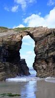 A stunning natural arch carved into towering sea cliffs on a sandy beach, with the ocean visible through the opening. photo