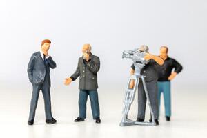 Miniature figure of a male journalist interviewing a businessman with a cameraman recording photo