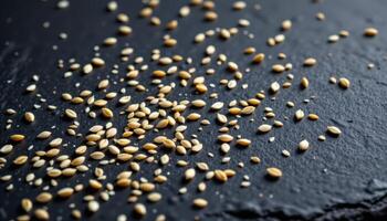close up view of sesame seeds sprinkled across a dark slate surface, each seed lit with directional shadow. photo