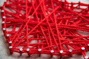 Creative use of vibrant red yarn intertwined around nails forms string art, showcasing textures and patterns. Techniques highlight craftsmanship and artistic expression. photo