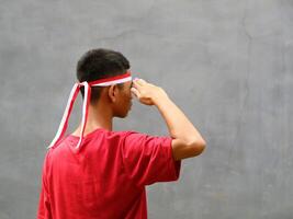Indonesian boy wearing red and white headband with salutes pose, celebrating Indonesian Independence Day photo