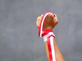 Hand with clenched fist wearing red and white ribbon on gray background during Indonesia's independence day celebration photo