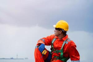 A man in a yellow helmet and orange jumpsuit is sitting on the ground photo
