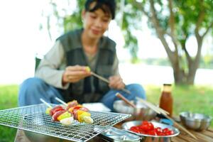 A woman is sitting on the grass and preparing food on a grill photo