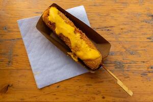 Delicious corn dog drizzled with cheese sauce served on wooden table at a fairground during sunny day photo