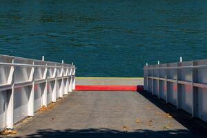 Scenic riverside dock leading to tranquil blue waters at midday under a clear sky in a serene natural setting photo