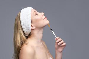 Young caucasian female applying face mask with brush in skincare routine. photo