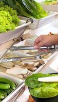 Hands picking mushrooms and greens from a buffet for Korean BBQ. Bright lighting highlights fresh produce in a vibrant setting video