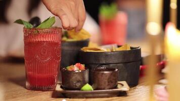 A hand dips chips into guacamole beside a vibrant drink, capturing a lively dining atmosphere with warm lighting video