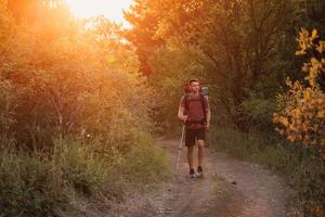 Hiker trekking through forest path with backpack and poles at warm sunset. Active lifestyle and adventure hiking concept. photo