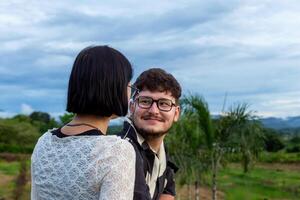 Man and woman at sunset in mountains. Young couple sharing joyful moment outdoors, surrounded by vibrant greenery and cloudy sky, capturing the essence of connection and happiness in natural setting photo