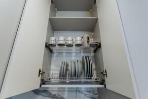 Picture a meticulously organized kitchen cabinet that is fully stocked with various plates, cups, and utensils, all expertly arranged to meet your cooking and dining needs efficiently photo