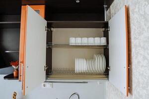 A beautifully designed kitchen cabinet that contains a wide variety of plates, cups, and kitchenware, all neatly arranged within it for easy access and effective organization photo
