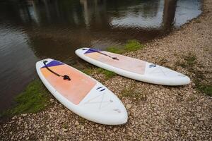 Two StandUp Paddleboards Are Resting Gently on the Shoreline by the Water, Awaiting Adventurers Who Seek Fun, Exercise, and Exploration in the Beauty of Nature and its Scenic Coastal Landscape photo
