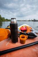 A person is comfortably sitting in a small boat, enjoying the serene surroundings, with a thermos filled with hot coffee and a cup ready to sip from. Its a peaceful moment on the water photo