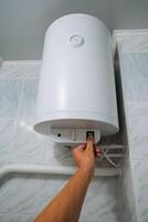 In a bathroom, an individual is deliberately pressing a button on a water heater, which is specifically designed to heat water for various purposes such as bathing, cleaning, and cooking photo