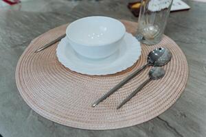 A beautifully arranged dining setting features an elegant placemat with a bowl, plate, spoons, and a crafted glass, creating a warm and inviting dining experience for all photo