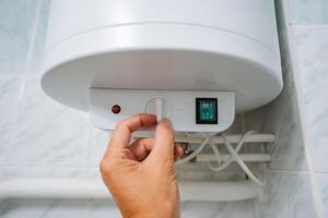 A person is in the process of turning on a water heater in a bathroom, preparing for a warm shower. The water heater is an essential home appliance that provides hot water for various needs photo