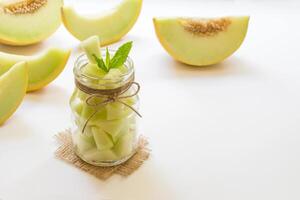 Left a jar with melon pieces on burlap napkin near cut slices of melon right empty place for text on a white background. Pieces of melon in a jar. Horizontal. Daylight. photo