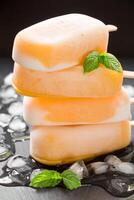 Three mango ice cream popsicles are neatly stacked on top of each other, resting on crushed ice. Fresh mint leaves garnish the popsicles, enhancing the vibrant colors and inviting a fresh summer vibe. photo