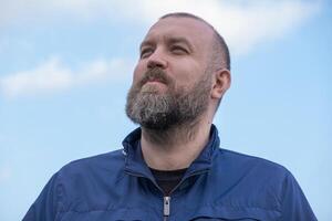 Man with beard looking up at a clear sky during a sunny day outdoors in a relaxed posture photo