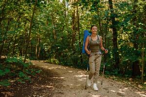 A woman enjoys trekking in a beautiful lush forest with a backpack and trekking poles photo
