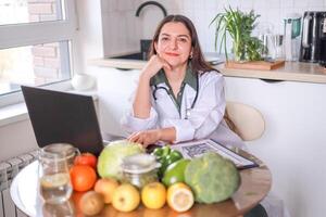 Nutritionist working with clients at a table full of fresh vegetables and fruits using a laptop and a tablet to record information. Health, wellness concept. photo