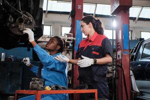 Two diverse female mechanic workers, Latino and Black coworkers fix automobile wheels, maintain car suspensions in garage station, technician engineering service jobs in vehicle transport industry. photo