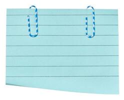 A rectangular sheet of light blue lined paper with two blue and white striped paper clips attached to the top. photo