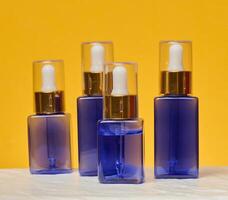 Transparent square blue bottles with gold caps and white pipettes photo