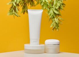Three white cosmetic products without labels tube, flat round jar and short round jar, stand on white table against bright yellow background photo