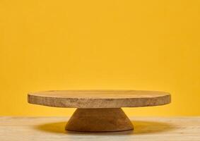 Wooden round podium on wooden table, on bright yellow background. Place for demonstration of products, cosmetics photo