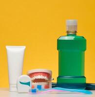 Oral hygiene kit including a tube of white toothpaste, dental floss, a green bottle of mouthwash and two toothbrushes, on a yellow background photo