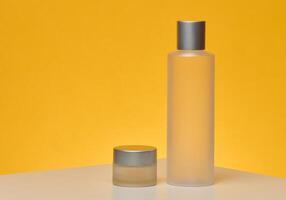 Two matte transparent cosmetic bottles with silver caps, a tall cylindrical one and a short round one, yellow background photo