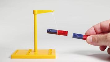 A hand manipulates magnets, demonstrating attraction and repulsion. Bright lighting highlights the magnetic forces in a controlled environment video