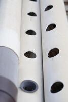 Along the white pipe, there are multiple evenly placed round holes. photo