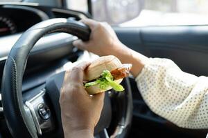 woman driver hold and eat hamburger in car, dangerous photo