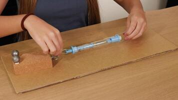 Hands pull a spring scale to measure friction on a cardboard surface using weights, highlighting physics principles video
