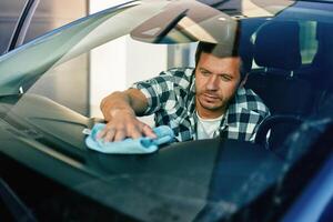 Man cleaning car dashboard with microfiber cloth while sitting inside vehicle photo