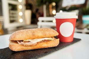 A sandwich with a red plastic glass of coffee on the table in a coffee shop. photo
