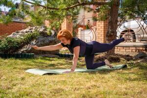 Woman doing stretching exercises on a mat in the park with focus on spine and mobility. Gentle fitness, body awareness, and healthy movement routine. High quality photo