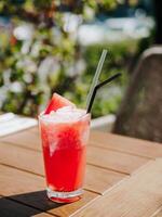 Fresh drink with watermelon, cold summer lemonade, healthy mocktail. Watermelon drink in sunny summer day shadows on wooden table background with copy space. Vertical. photo