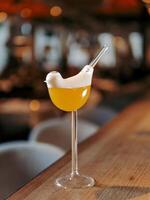 Tommy D Sour Cocktail in bird high stem cocktail glass on bar counter background with bokeh. Yellow alcohol Tommy Dee Sour cocktail made with whiskey, egg white, angostura, passion fruit syrup photo