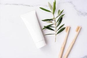 White plastic tube without label, bamboo toothbrushes and olive branch on white background photo