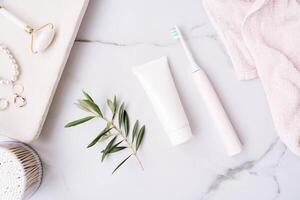 Top view of plastic tube without label, electric toothbrush and olive branch on white bath background photo