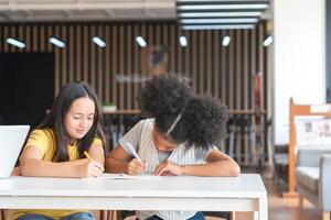 Diverse Young Girls Studying Together at School, Two Elementary Students Focused on Writing in Classroom, Kids Collaborating on Homework at a Desk photo