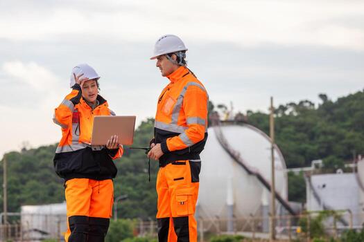 Engineers Collaborating at Industrial Site with Storage Tanks, Team of Engineers Conducting Operations at Oil Storage Field Industrial Site, Industrial Workers with Laptop Communicating at Site photo