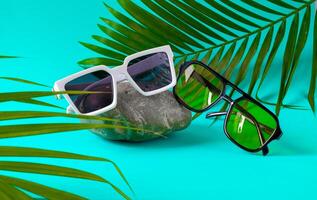 Trendy sunglasses on rock with palm leaves. photo