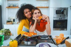 Two women are posing for a picture in a kitchen with a pizza on the table photo