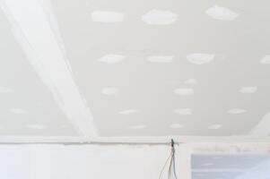 Preparing gypsum board ceiling inside residential building during interior renovation showing electrical wire along smooth edges plastering work underway photo